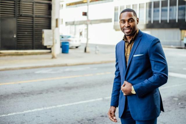 African American man in a suit, standing near a street smiling. Photo by Tamarcus Brown on Unsplash